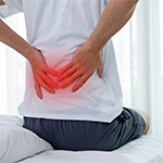 a person suffering from back pain holding their back.