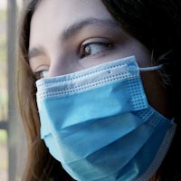 a woman wearing a surgical mask and looking out a window