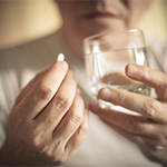A person holding a glass of water and a pill